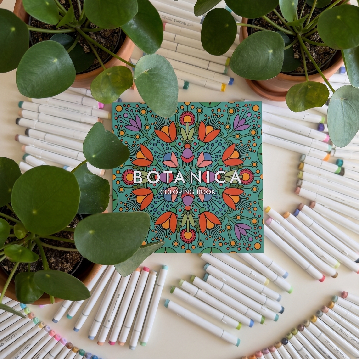 Coloring book titled 'Botanica' surrounded by coloring markers and potted plants.