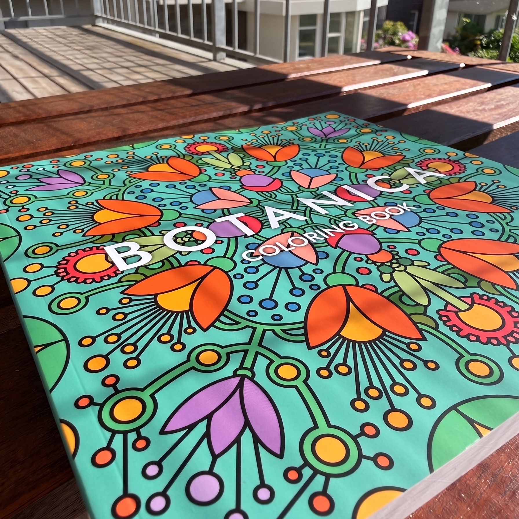 Front cover of the square BOTANICA floral coloring book by Luka Torkovic on a rustic wooden outdoor table.