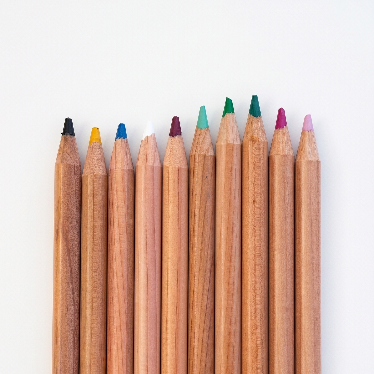 A row of nine wooden Caran d'Ache Luminance colored pencils with visible white brand labels on a plain white studio background.